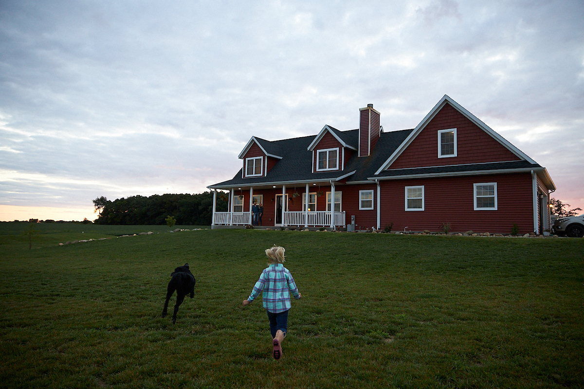 Country home with porch Rural family home for sale Safe family neighborhood Spacious front yard house Red farmhouse exterior Sunset home photography Dog-friendly homes in the countryside Peaceful residential property